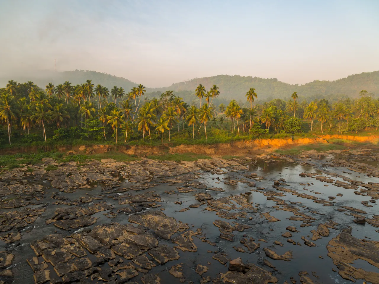 Goldenes Abendlicht über dem felsigen Maha Oya, eingerahmt von palmenbewachsenen Hügeln in Sri Lanka.